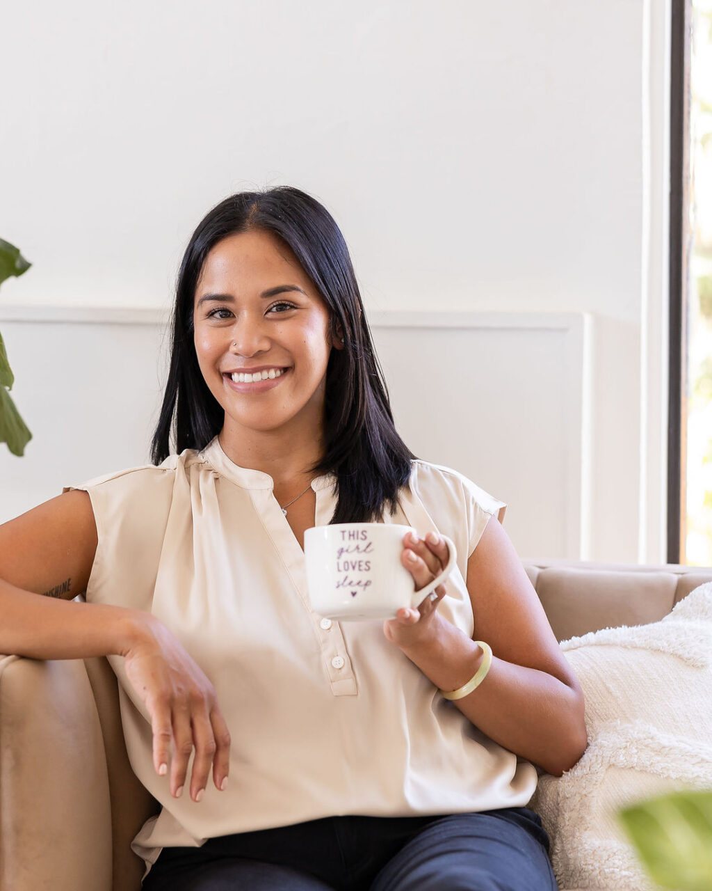 Dr. Monee Dulay smiling on a sofa holding a mug